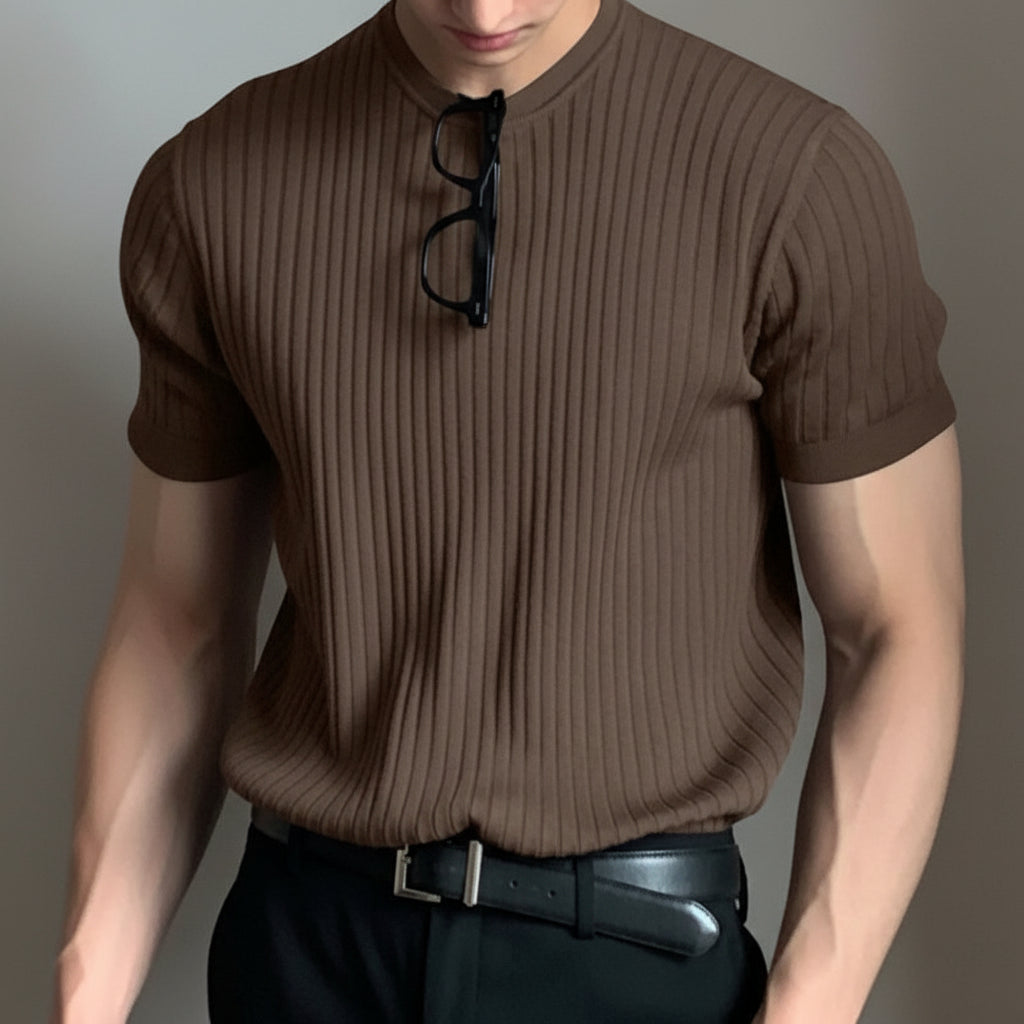 Person wearing a brown ribbed shirt with glasses on their shirt collar against a neutral background