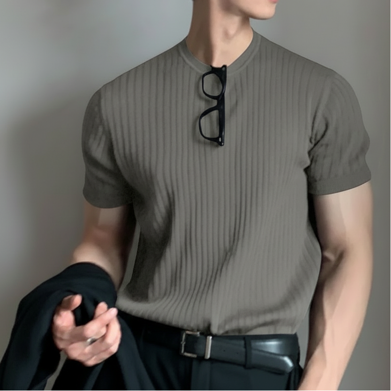 Person wearing a gray t-shirt with a pair of glasses hanging from it against a plain background